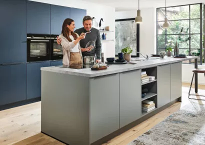 Frau und Mann stehen an einer Kücheninsel und kochen gemeinsam.