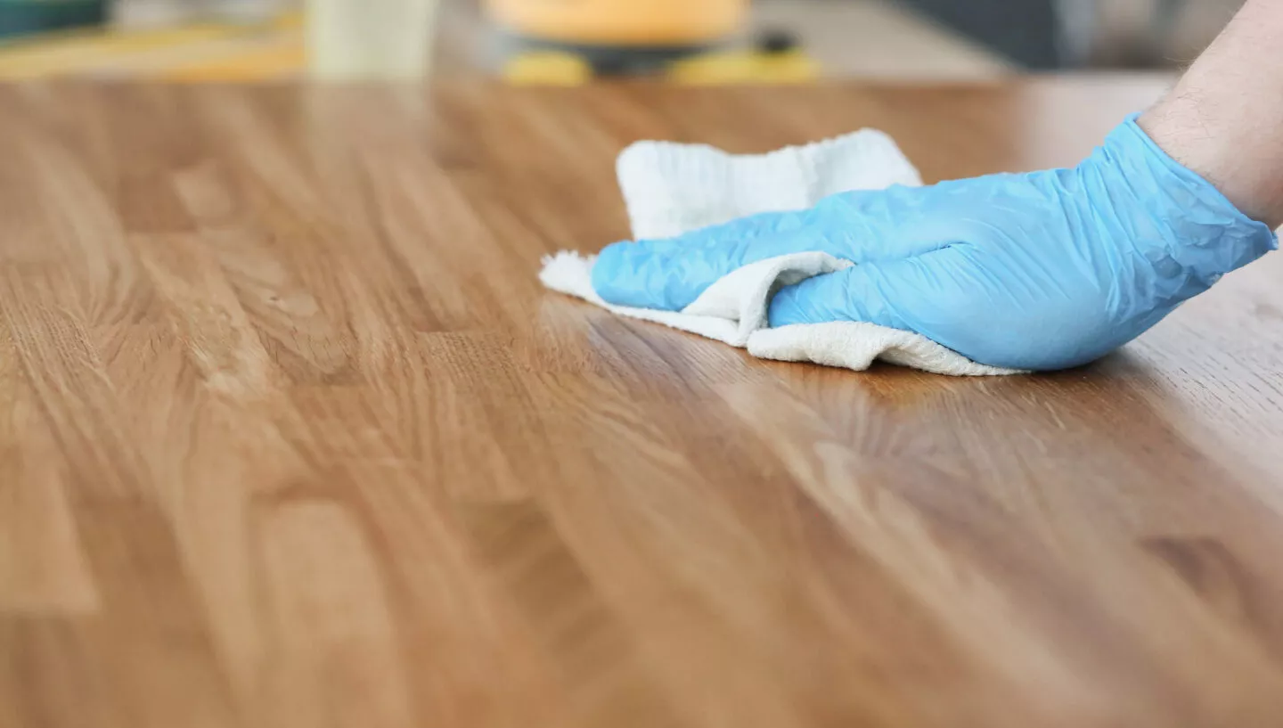 Naturmaterialien pflegen: Eine Hand fährt mit einem Lappen über eine Holzoberfläche.