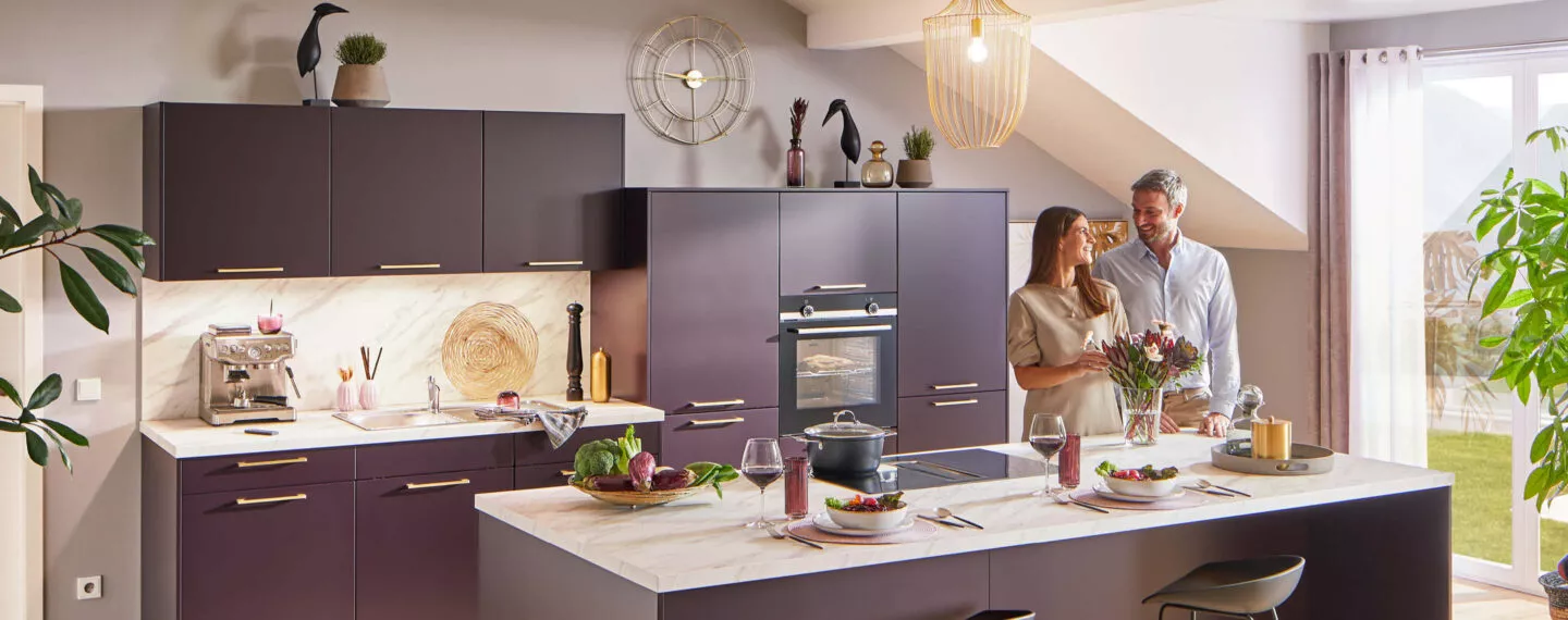 Glückliches Pärchen in einer lila farbenen Küche mit weißer Steinarbeitsplatte.