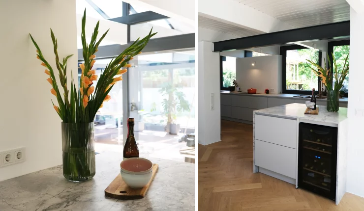 Kücheninsel in heller Steinoptik mit dekorativer Blumenvase, daneben moderne Küchenzeile und integrierter Weinkühlschrank.