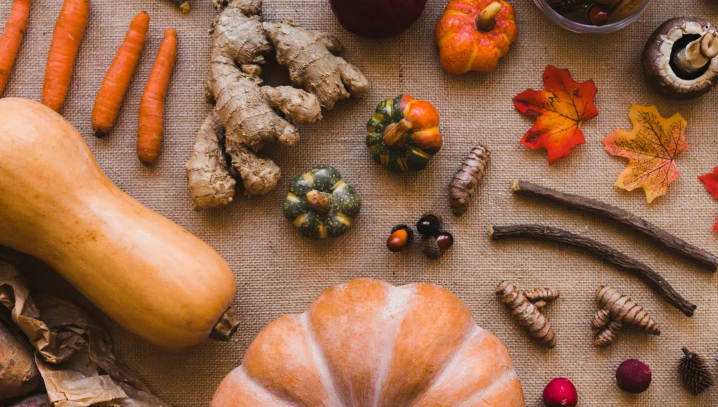Herbstliche Zutaten mit Kürbis, Karotten, Ingwer, roter Zwiebel, Pilzen, Nüssen und Wurzelgemüse auf natürlichem Stoff arrangiert – Inspiration für saisonale Herbstrezepte in der Küche.