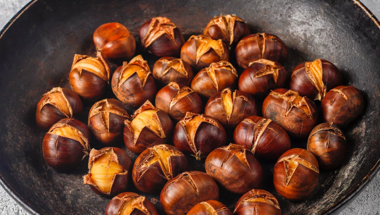 Geröstete Kastanien in einer dunklen Pfanne auf heller Arbeitsfläche – saisonale Herbstzutat für warme, herzhafte Gerichte und herbstliche Rezepte.