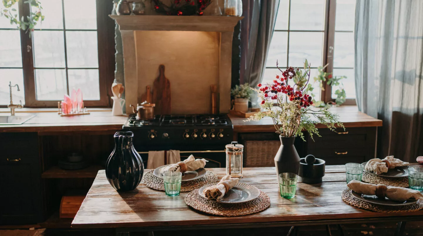 Wohnliche Küche mit dunklen Holzfronten und gedecktem Holztisch, dekoriert mit Textilien, Naturmaterialien und herbstlichen Zweigen für eine gemütliche Atmosphäre.